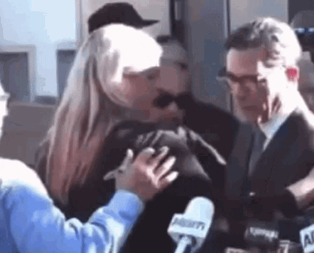a woman is kissing a man in front of a microphone while a man in a suit looks on .