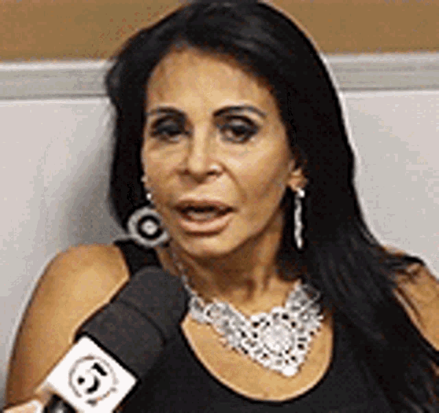 a woman wearing a necklace and earrings is talking into a microphone with the number 6 on it .