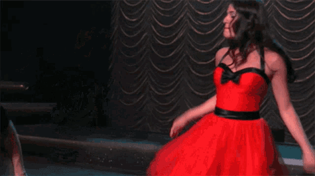 a woman in a red dress is dancing in front of a green curtain