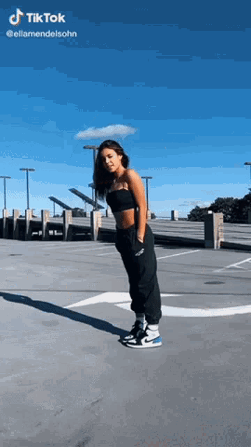 a woman is standing in a parking lot wearing a black top and black pants