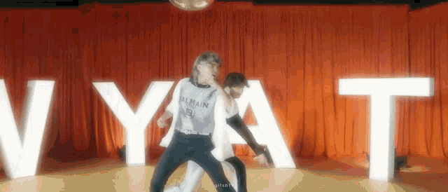 a couple of people are dancing on a stage in front of a red curtain with a disco ball .
