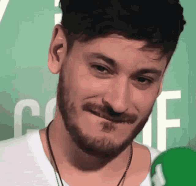 a man with a beard is making a funny face in front of a green sign that says coffe