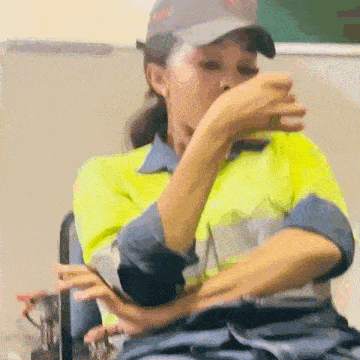 a woman in a yellow shirt and hat is sitting in a chair and covering her mouth with her hand .