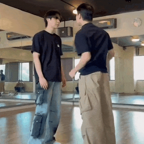 two men are standing next to each other in a dance studio talking to each other .