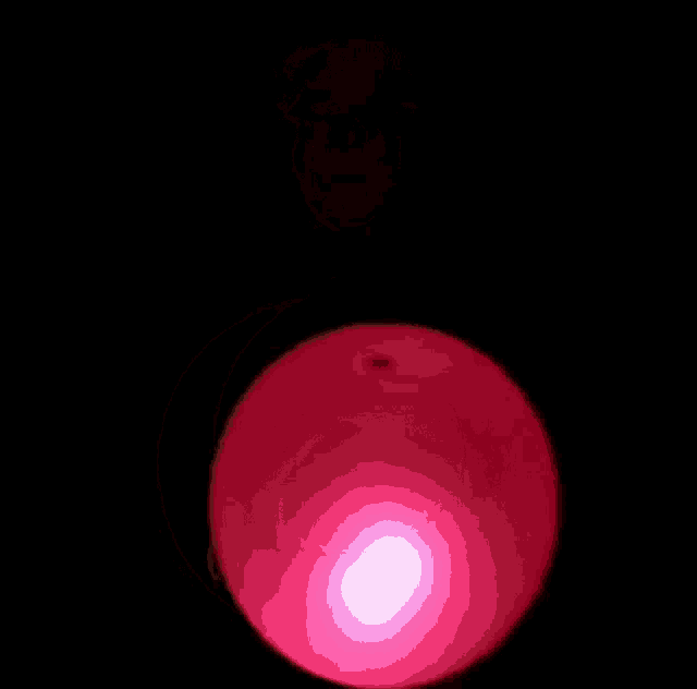 a pink balloon is glowing in the dark against a black background .