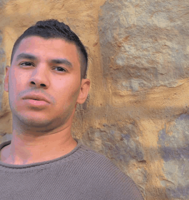 a man leaning against a wall with a sweater on