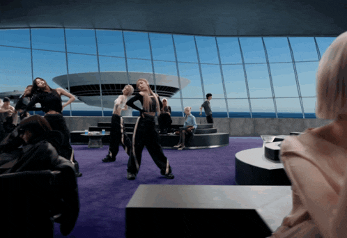 a group of people dancing in a room with a large window