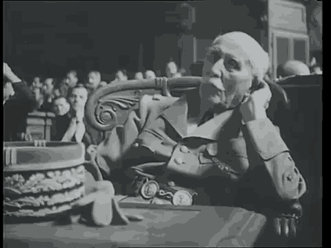 a man with a mustache is sitting at a table in front of a crowd