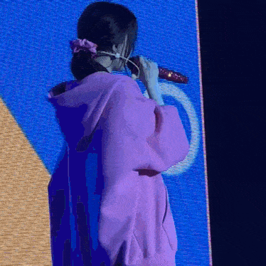 a woman wearing a pink hoodie is singing into a microphone