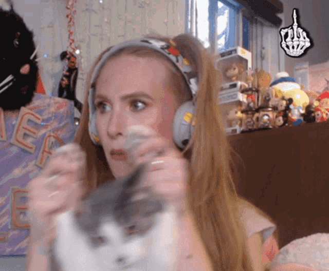 a woman wearing headphones holds a cat in front of a peace sign