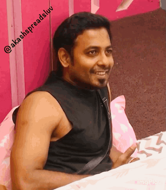 a man in a black tank top is smiling in front of a pink wall that says @akashspreadslv