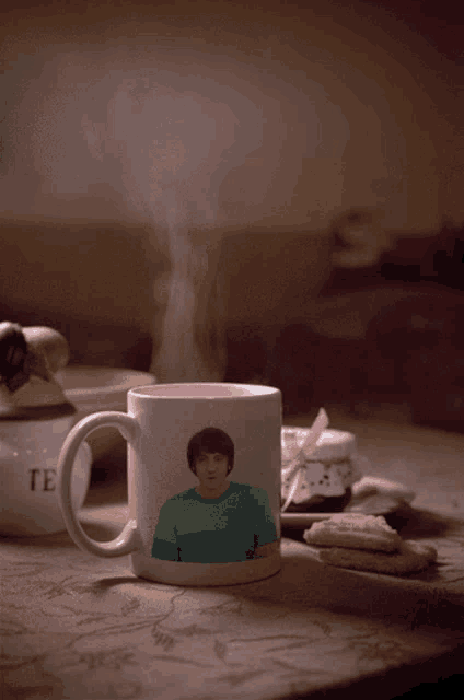 a mug with a man on it sits on a table next to a tea jar
