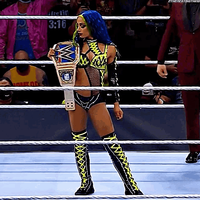 a woman with blue hair is standing in a wrestling ring holding a wwe championship belt .