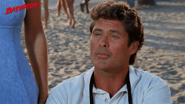 a man sitting on a beach with the word baywatch on the bottom right