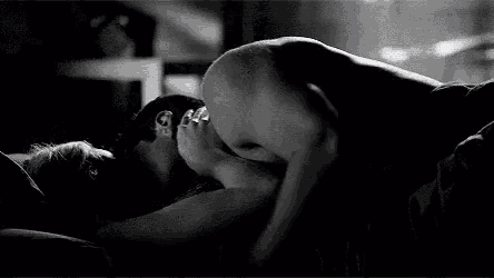 a black and white photo of a man and a woman kissing on a bed .
