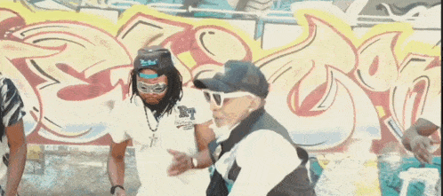 a group of people are dancing in front of a graffiti wall .