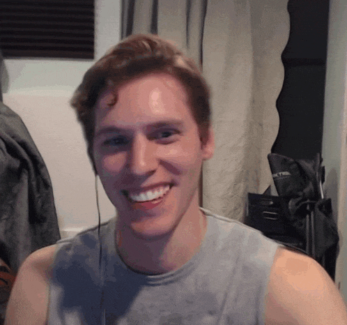a man wearing headphones and a tank top smiles for the camera