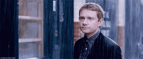 a man in a suit is standing in the rain and looking at the camera .