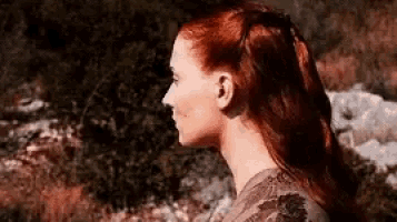 a close up of a woman 's face with red hair standing in a field .