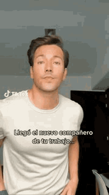 a man in a white t-shirt is standing in a room and making a funny face .