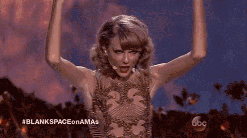 taylor swift is standing on a stage with her arms in the air in front of a fire .