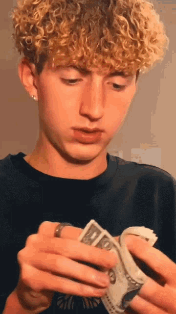 a young man with curly hair is holding a bunch of money