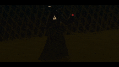 a silhouette of a person in a black coat holding a red object in a dark room .