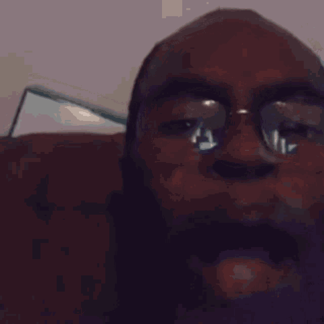 a man wearing glasses is sitting on a couch with his mouth wide open .