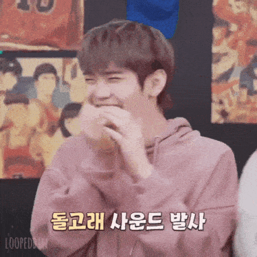 a man in a pink hoodie is laughing in front of a poster with the number 10 on it .