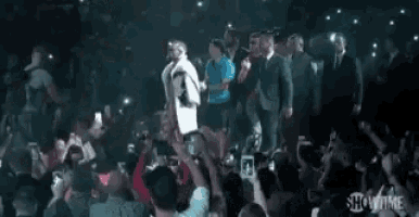 a man in a white coat is walking through a crowd of people in a boxing ring .