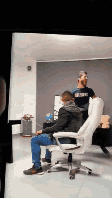 a man wearing a black shirt that says brooklyn is standing next to a man sitting in a white chair