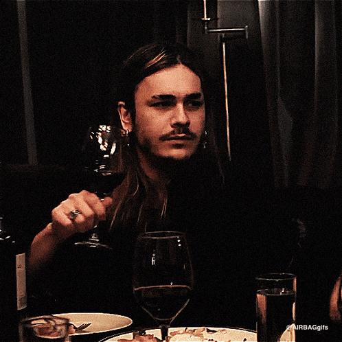 a man with long hair holds a glass of wine