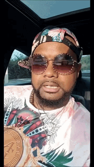 a man wearing sunglasses and a hat with the letter a on it is sitting in a car
