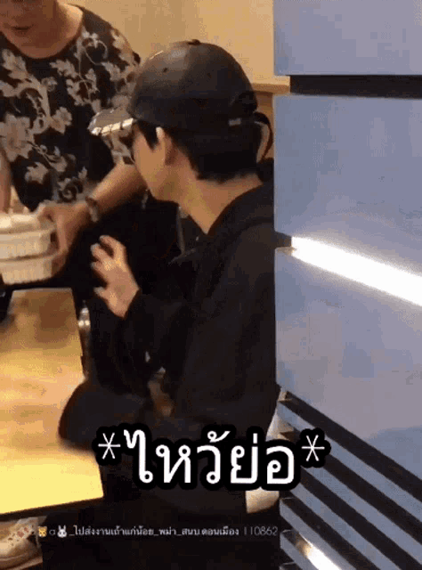 a man wearing a black hat is sitting at a table with a sticker that says * t *