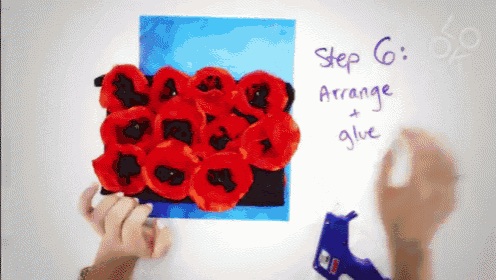 a person is holding a piece of paper with red flowers and a glue gun in front of them