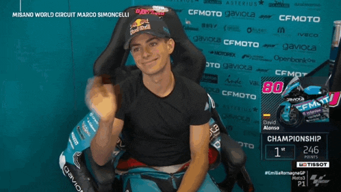 a man wearing a red bull hat is sitting in a chair