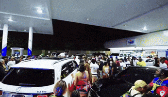 a crowd of people are gathered at a gas station including a white mercedes