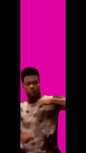 a man in a tie dye shirt is standing in front of a pink background and holding something in his hands .
