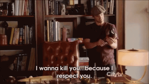 a man in a hat stands in front of a bookshelf and says " i wanna kill you "