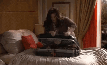 a woman is packing a suitcase on a bed in a bedroom