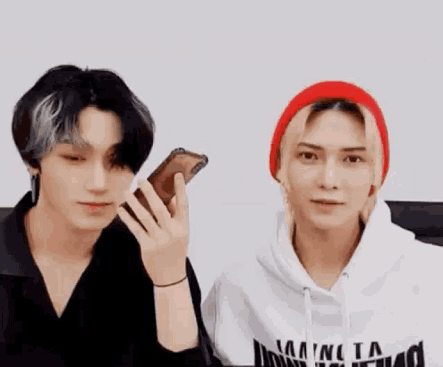 two young men are sitting next to each other looking at their phones .