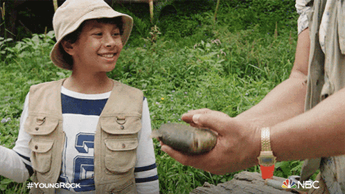 a young boy wearing a hat and vest is holding a rock and smiling at a man