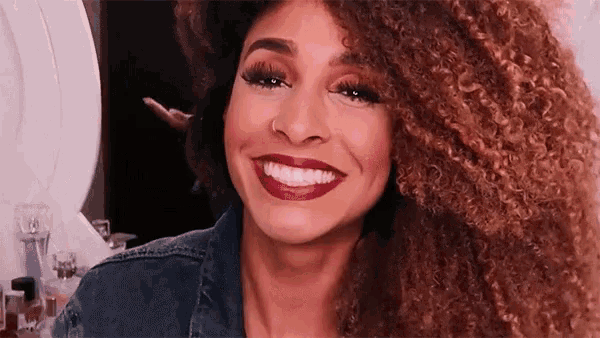 a woman with curly hair and red lipstick smiles