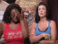 two women are standing next to each other with their arms crossed and one is covering her face with her hand .
