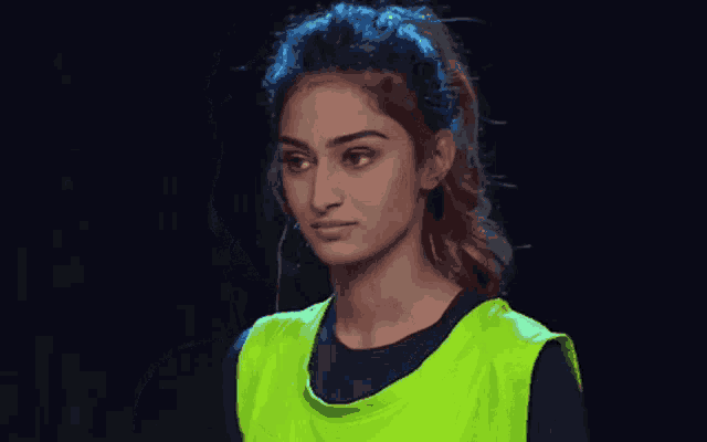 a woman wearing a green vest and a black shirt looks at the camera .