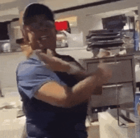a woman in a blue scrub top is standing in a kitchen with her hands in the air .