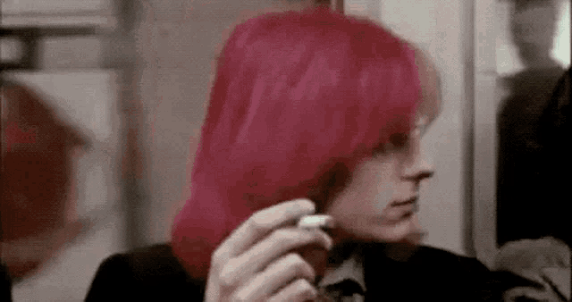 a woman with bright pink hair is holding a cigarette in her hand .
