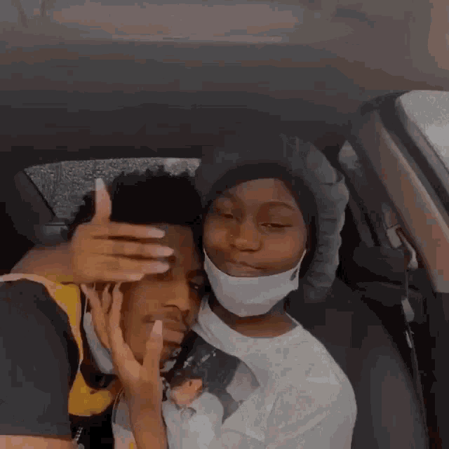 a man and a woman are sitting in a car . the woman is wearing a mask .