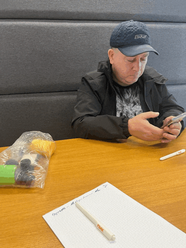 a man sitting at a table looking at his phone with a pen that says ' snuggle ' on it