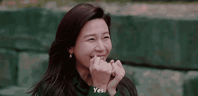 a woman is smiling and making a heart shape with her hands while sitting on a bench .
